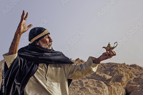 An old Arabic sorcerer holds an Aladdin's lamp and conjures.
