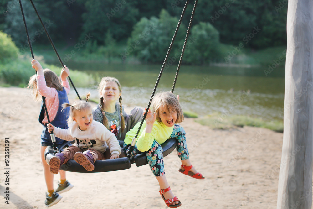 four children swinging on wicker swing on playground in park by lake, Sand and children's summer vacation with friends