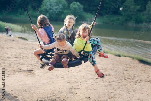 four children swinging on wicker swing on playground in park by lake, Sand and children's summer vacation with friends