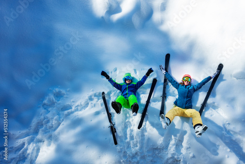 Mother and son lay in snow with ski lift, dangle legs