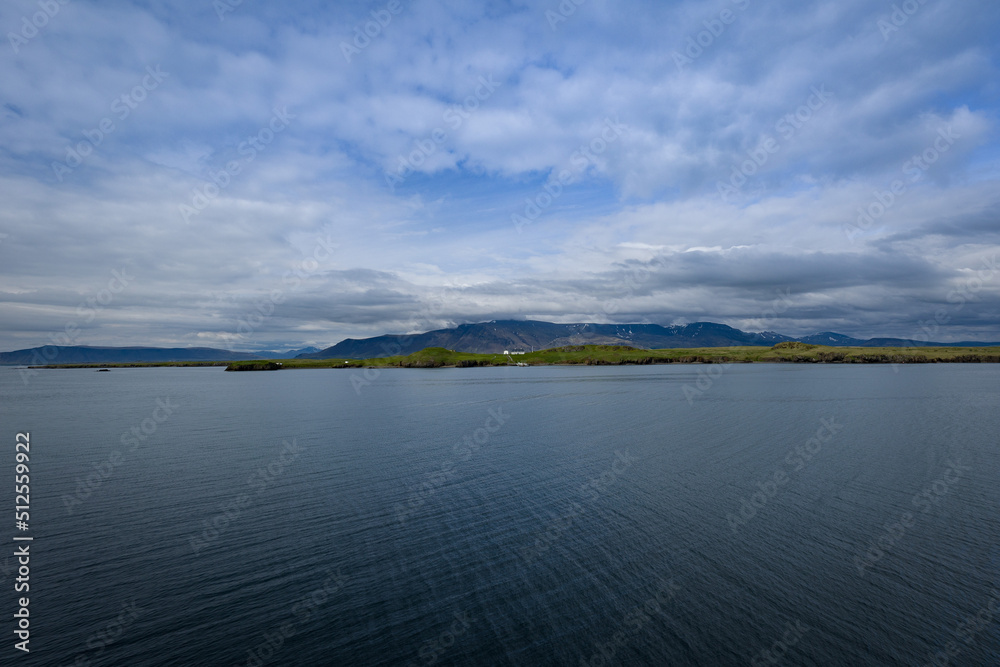 Body of water on the bottom and dramatic cloudscape on the top with a strip of land with a house in between in an Icelandic landscape