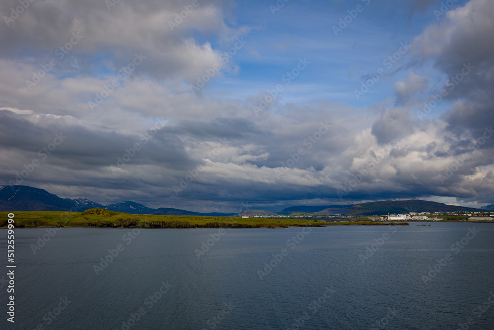 Dramatic skies over Reykjavik, Iceland harbor with snow covered mountains on the strip of land on the distance
