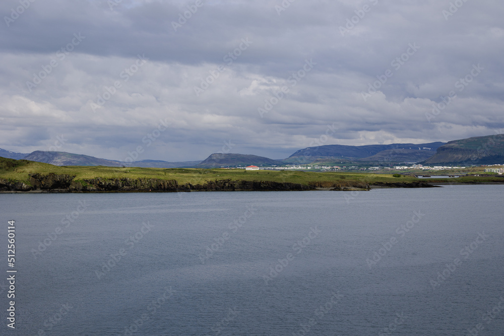 Clear and calm waters of Reykjavik harbor close to the city port. Icelandic mountain ranges displayed on the small strip of land in the middle of the frame.