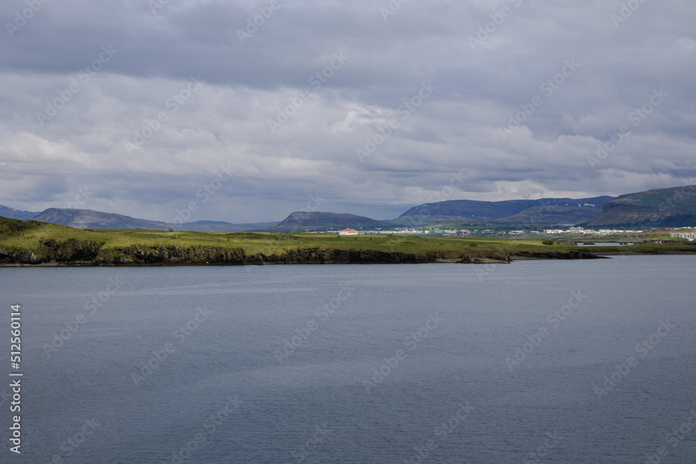 Clear and calm waters of Reykjavik harbor close to the city port. Icelandic mountain ranges displayed on the small strip of land in the middle of the frame. Clear and calm waters of Reykjavik harbor close to the city port. Icelandic mountain ranges displayed on the small strip of land in the middle of the frame.