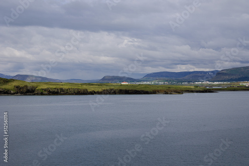 Clear and calm waters of Reykjavik harbor close to the city port. Icelandic mountain ranges displayed on the small strip of land in the middle of the frame.
