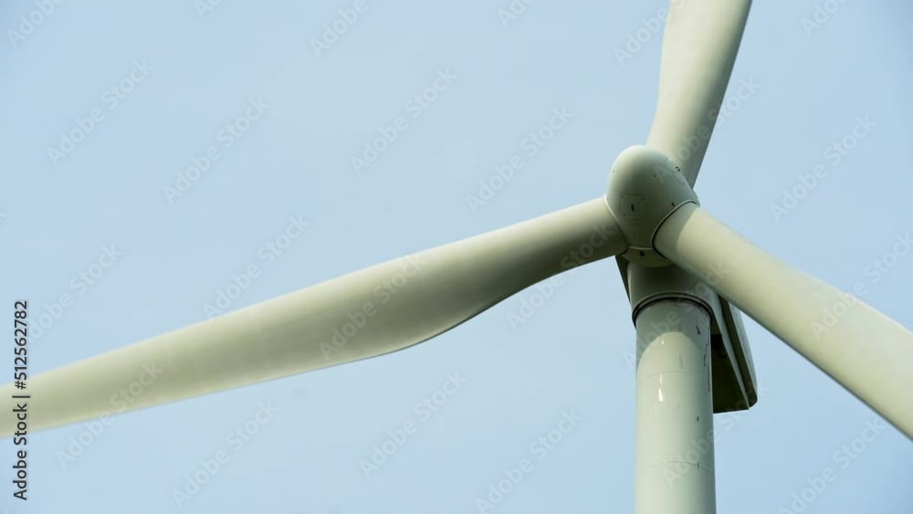 Close-up view of a modern windmill against a blue sky. The white blades of the wind turbine. Clean and renewable energy production. pipe and supporting base windmill close up Close-up view of a modern windmill against a blue sky. The white blades of the wind turbine. Clean and renewable energy production. pipe and supporting base windmill close up