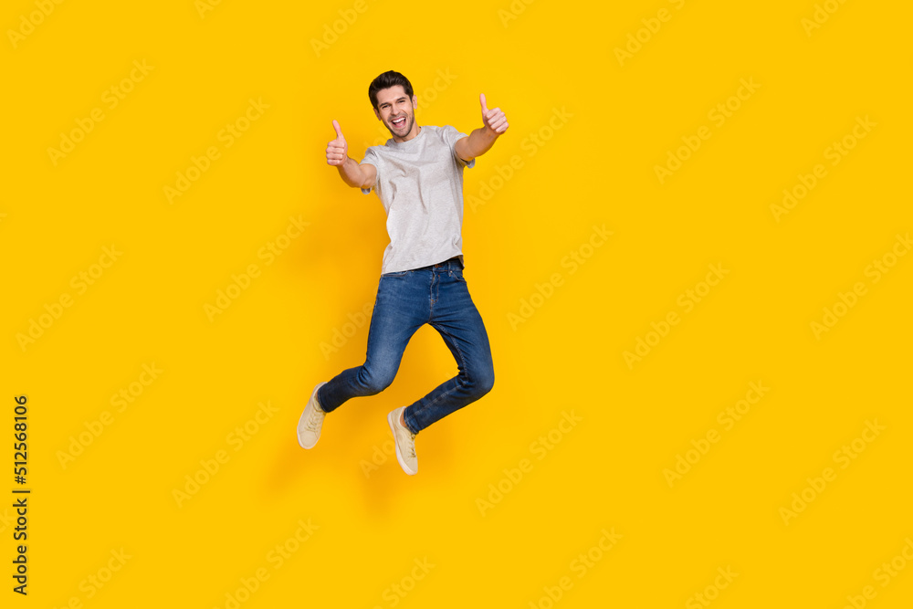 Full length body size view of attractive cheerful guy jumping giving two thumbup isolated over bright yellow color background
