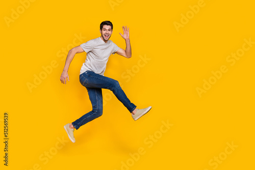 Full size photo of cool brunet young guy run wear t-shirt jeans shoes isolated on yellow background