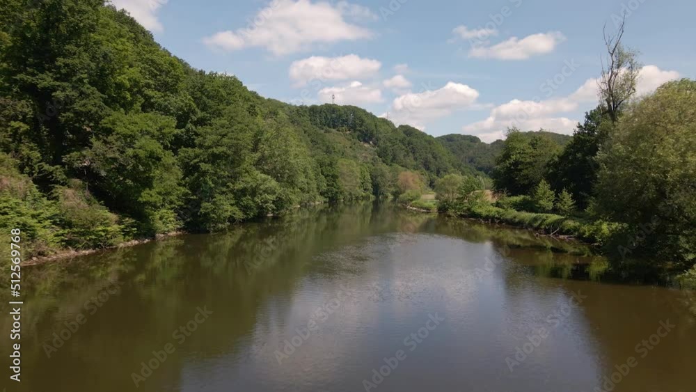 Lush, green nature surrounding a calm, brown river in North Rhine Westphalia, Germany on a sunny summer day. Ascending aerial fly over shot Lush, green nature surrounding a calm, brown river in North Rhine Westphalia, Germany on a sunny summer day. Ascending aerial fly over shot