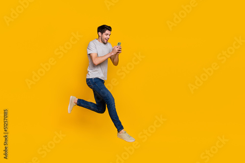 Full length body size view of attractive cheerful guy jumping using device running isolated over vivid yellow color background
