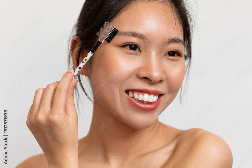 Beautiful korean lady brushing brows and applying eyebrow mascara, using decorative makeup, white background Beautiful korean lady brushing brows and applying eyebrow mascara, using decorative makeup, white background