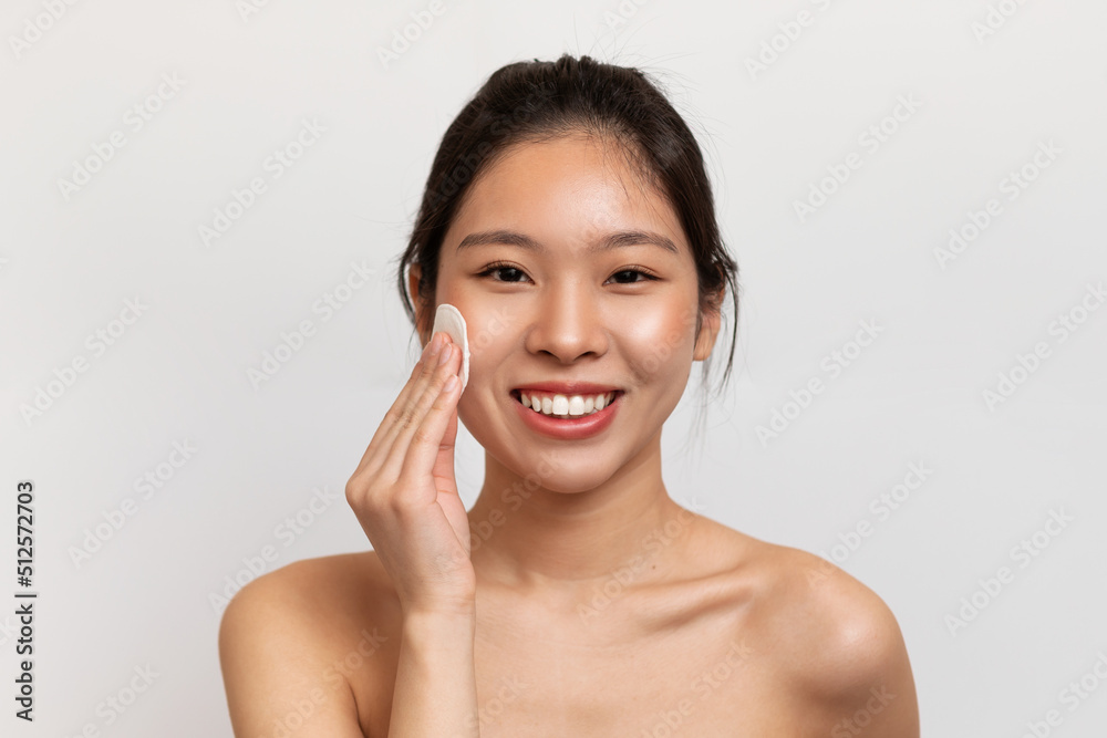 Skincare concept. Happy korean woman cleaning face with cotton pad, enjoying morning beauty routine Skincare concept. Happy korean woman cleaning face with cotton pad, enjoying morning beauty routine