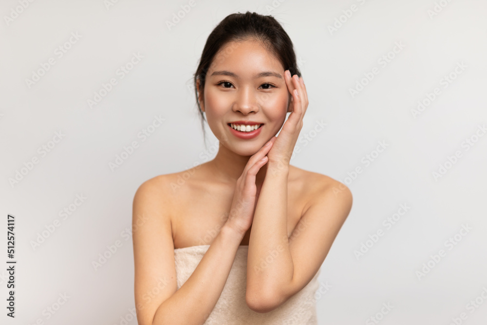Cosmetology and skin care concept. Portrait of young korean lady holding her hand near face and smiling at camera Cosmetology and skin care concept. Portrait of young korean lady holding her hand near face and smiling at camera