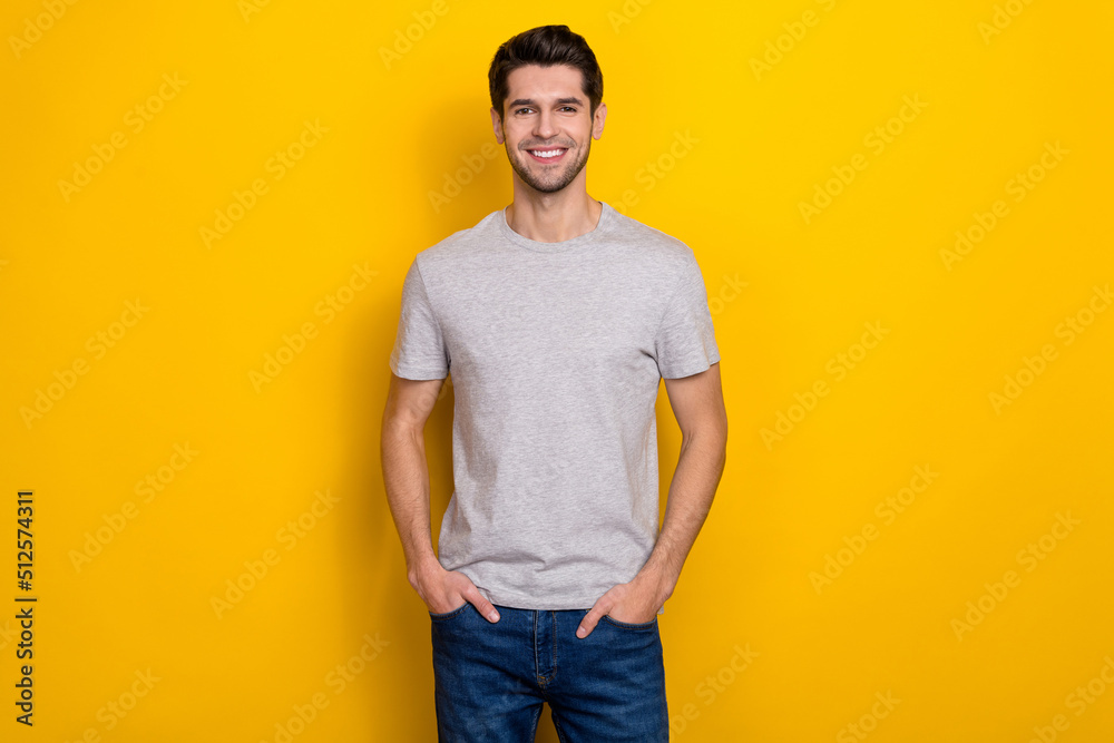 Photo of nice brunet millennial guy wear grey t-shirt jeans isolated on yellow color background Photo of nice brunet millennial guy wear grey t-shirt jeans isolated on yellow color background