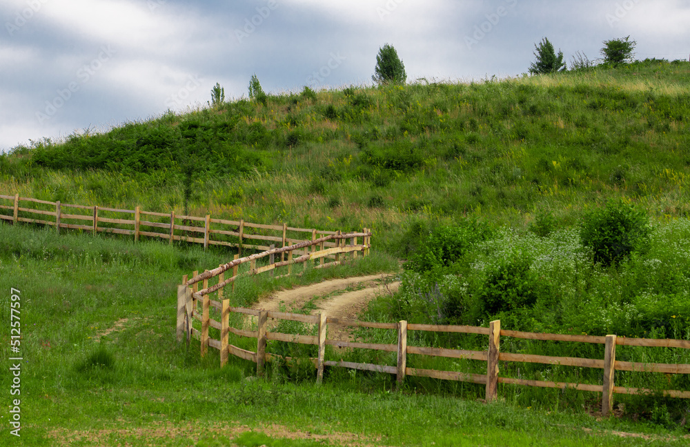 a dirt road near a wooden fence on a hillside