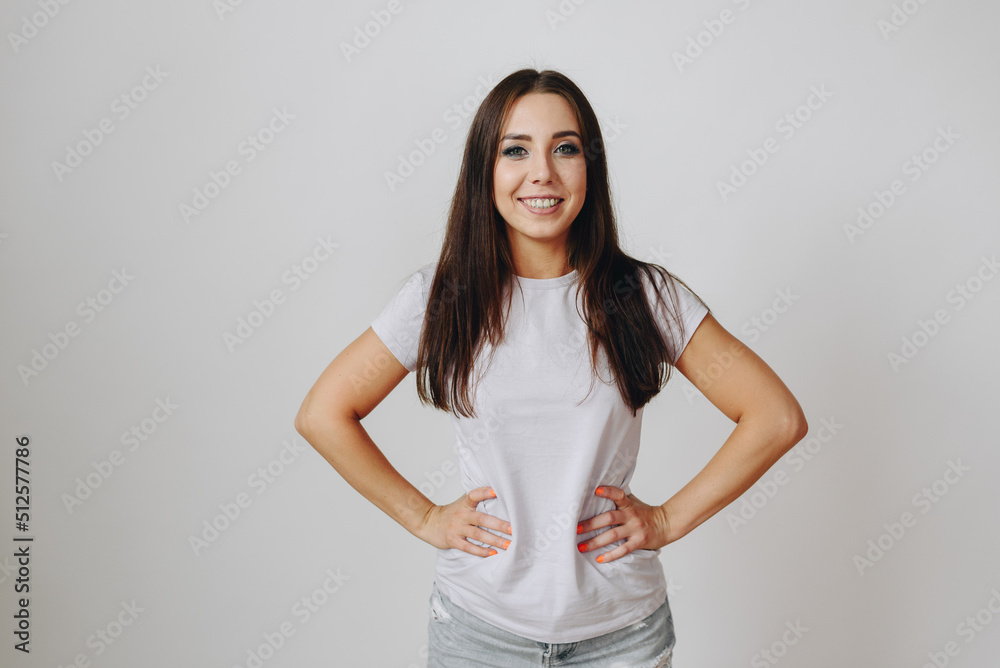 young brunette Woman in White T-shirt stands against backdrop of White Wall. Dentistry concept. young brunette Woman in White T-shirt stands against backdrop of White Wall. Dentistry concept.