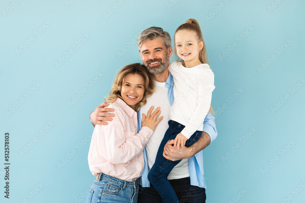 Man Holding Daughter In Arms Embracing Wife On Blue Background