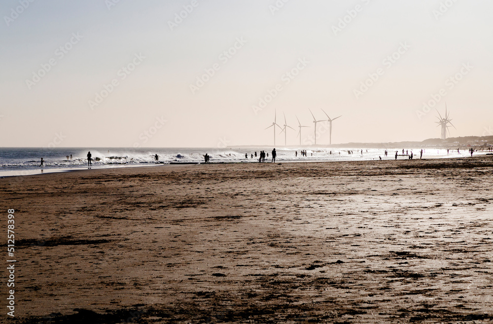 Necochea, Argentina. The beach at sunset with people and wind turbine power generators silhouetted by the backlight of sunlight. 