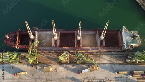 Aerial view of big cargo ship bulk carrier is loaded with grain of wheat in port at sunset