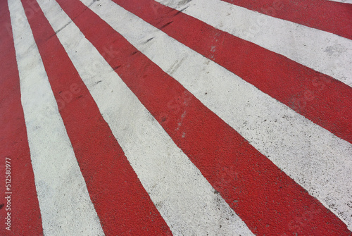 A flag with bright red and white diagonal stripes. Road markings on asphalt. Striped texture for revolutionary background. The rays of the rising sun fall from left to right from the upper left corner © brajianni