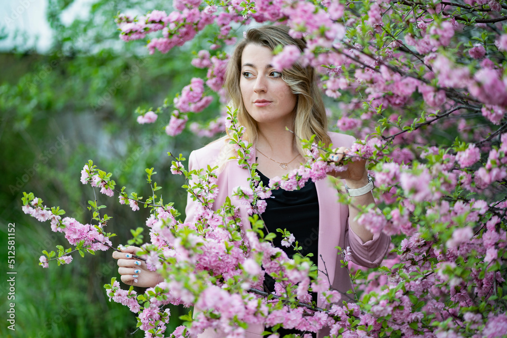 A very beautiful blonde in a pink jacket and a black blouse sensually poses standing among the flowers of cherry blossoms A very beautiful blonde in a pink jacket and a black blouse sensually poses standing among the flowers of cherry blossoms