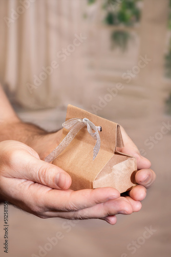 The gift is wrapped in kraft paper in the hands of a man. Mother's Day concept, or Valentine's Day. Vertical photo.