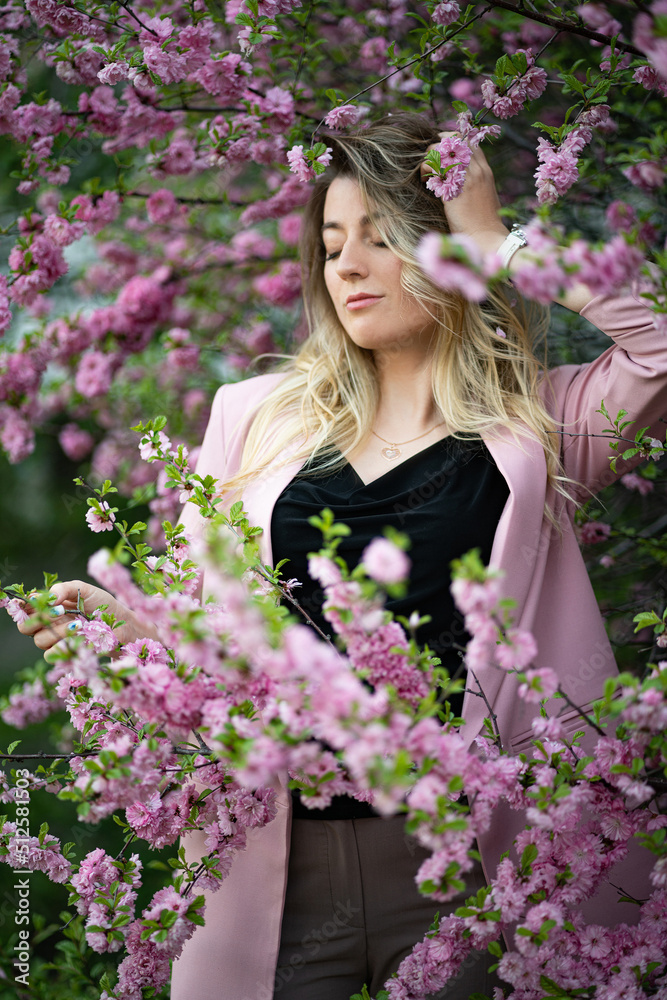 A very beautiful blonde in a pink jacket and a black blouse sensually poses standing among the flowers of cherry blossoms with her eyes closed. Goddess of nature or earth A very beautiful blonde in a pink jacket and a black blouse sensually poses standing among the flowers of cherry blossoms with her eyes closed. Goddess of nature or earth