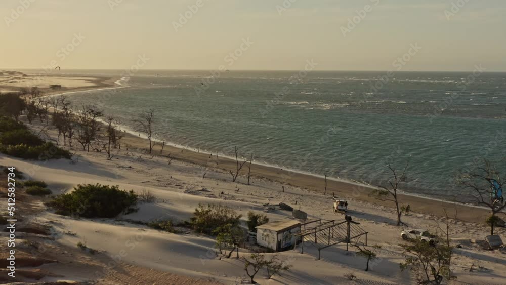 Pickup trucks drive along bay with kite surfers playing in sunset glow; drone Pickup trucks drive along bay with kite surfers playing in sunset glow; drone