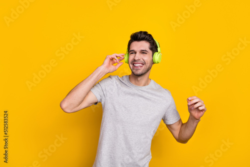 Photo of funny brunet young guy enjoy music look up wear earphones grey t-shirt isolated on yellow color background