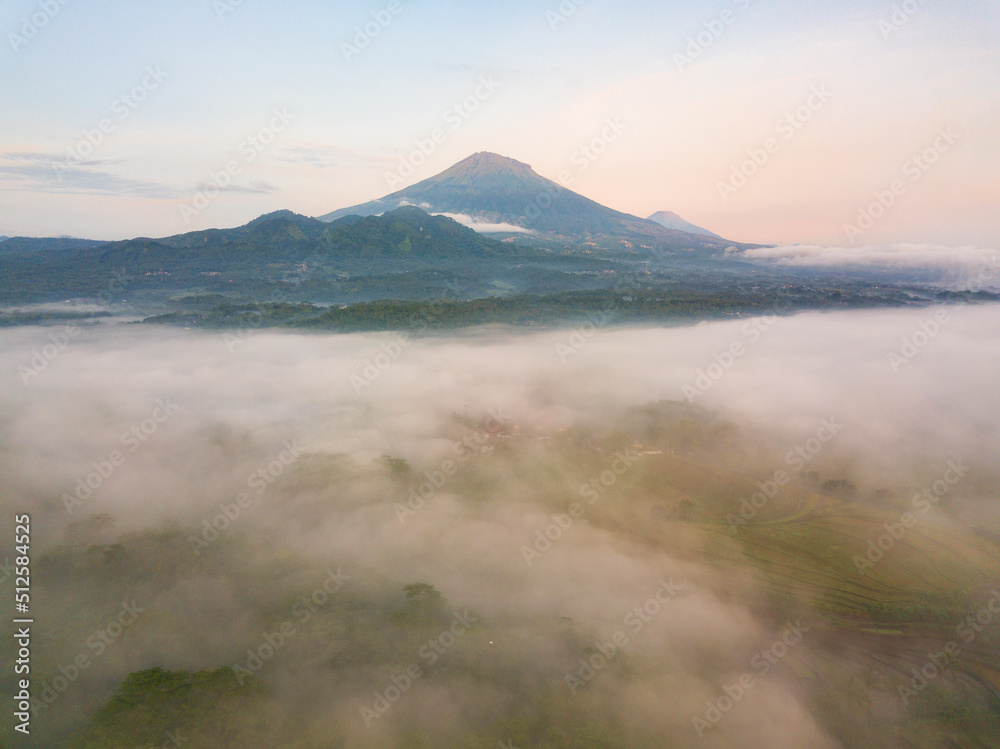 Drone photo of Mount Sumbing with sea of fog covered the land of plantation and trees in the morning. Central Java, Indonesia