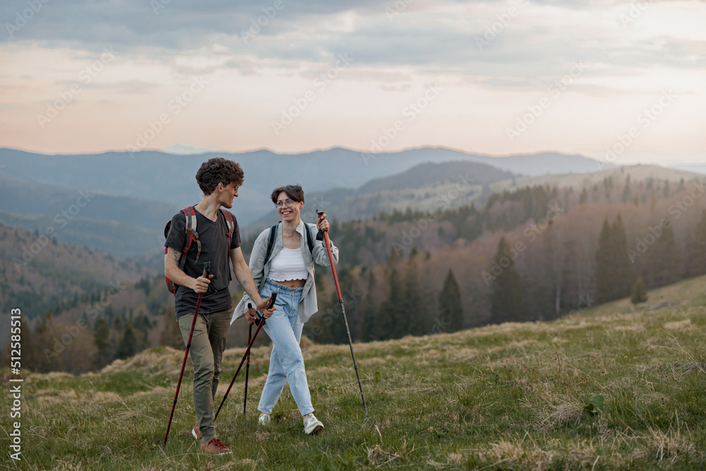 Portrait of young happy couple of tourists walking the mountains chain with sticks. Landscape.