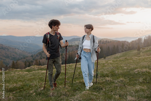 Caucasian man and woman hikers trekking with walking sticks in mountains with beautiful view. © Kostiantyn