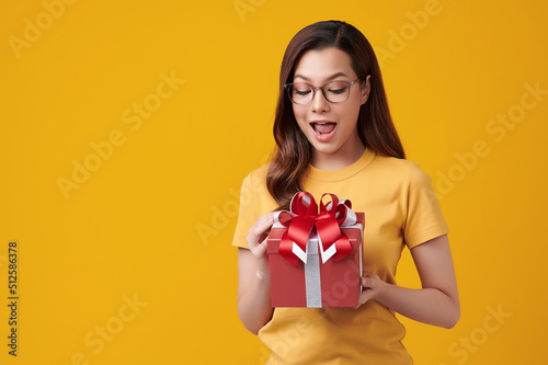 Happy pretty young woman holding gift box on yellow background, blank copy space for your advertising content. © kitthanes