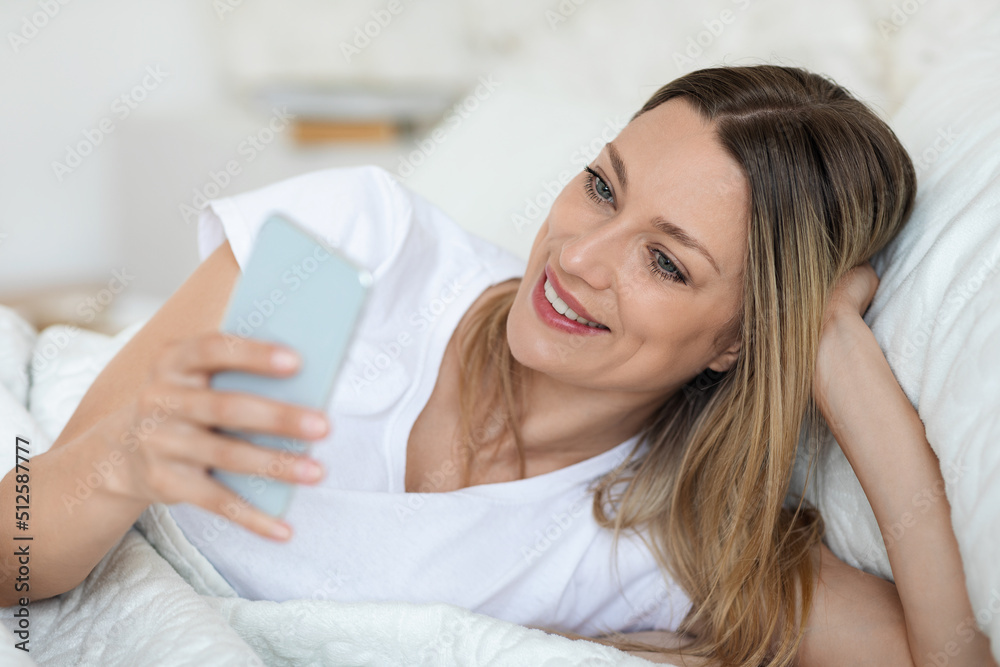 Happy woman checking smartphone in bed, closeup photo