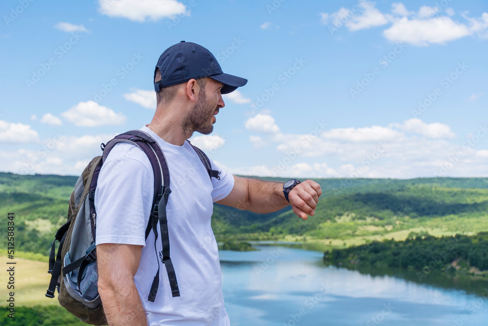 Man with Backpack Looking his Smartwatch and Counting Burned Calories in the Mountain  . Heart rate checking on smartwatch 