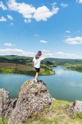 Young beautiful traveler woman sitting on a rock above lake .Traveling in the summer nature