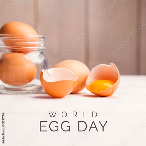 Digital composite of brown eggs in jar and broken egg on table with world egg day text, copy space