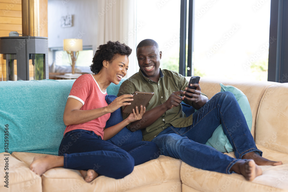 Happy african american mid adult couple using digital tablet and smart phone on sofa in living room Happy african american mid adult couple using digital tablet and smart phone on sofa in living room