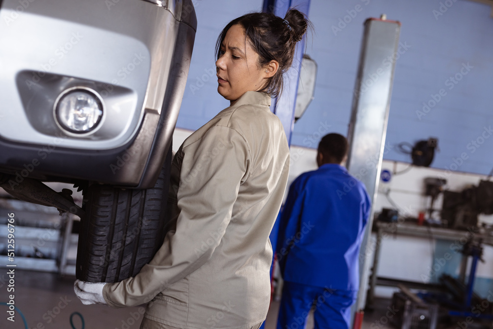 Mid adult asian female mechanic fixing car's tire in workshop with colleague in background Mid adult asian female mechanic fixing car's tire in workshop with colleague in background