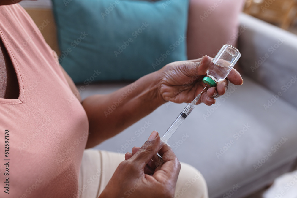 Midsection of african american senior woman holding vial and syringe while sitting on sofa at home Midsection of african american senior woman holding vial and syringe while sitting on sofa at home