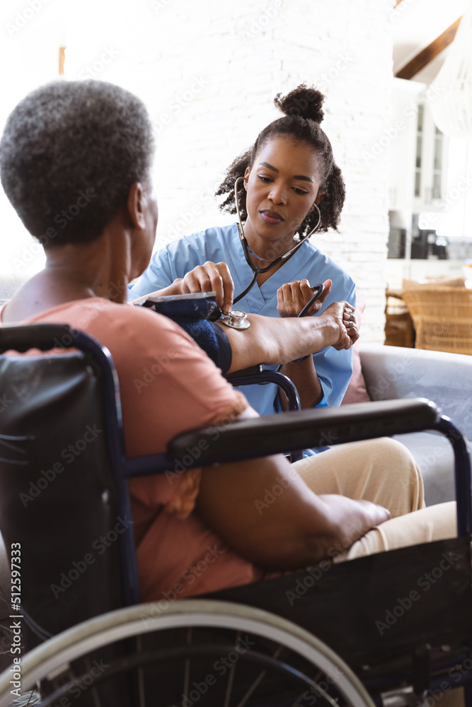 African american doctor examining senior woman's blood pressure with gauge and stethoscope at home African american doctor examining senior woman's blood pressure with gauge and stethoscope at home