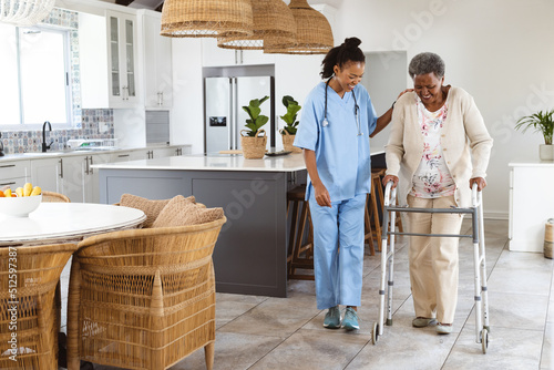 African american female doctor assisting senior patient in walking with walker at home photo