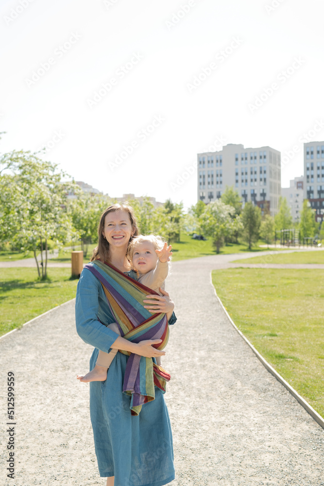 Smiling Mother Carrying Baby In Shawl Sling At Park Smiling Mother Carrying Baby In Shawl Sling At Park