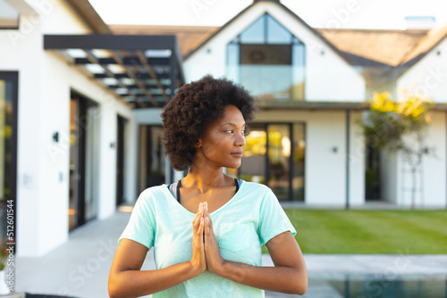 Afro young african american woman with hands clasped practicing yoga in backyard photo