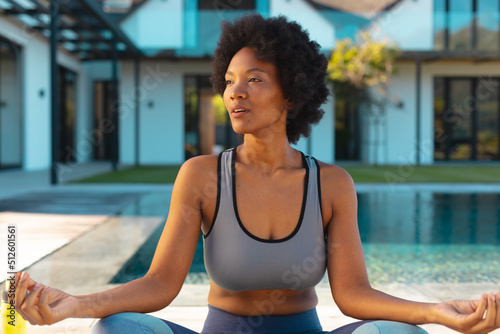 African american afro young woman looking away while practicing yoga on poolside