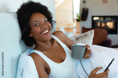 Cheerful young african american afro woman looking away while holding smart phone and coffee cup
