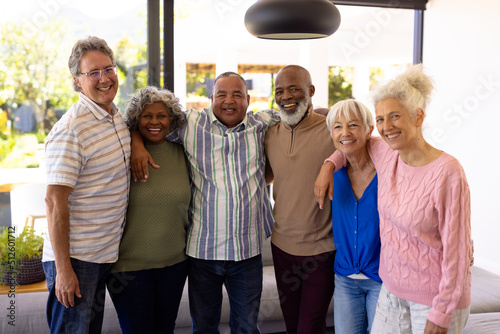 Portrait of multiracial cheerful senior friends with arms around standing in nursing home