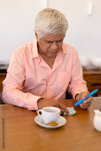 Senior biracial man with coffee cup and cookie on dining table playing bingo in nursing home
