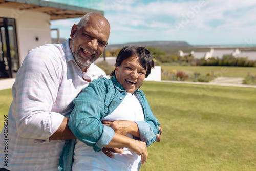 Portrait of cheerful biracial senior friends laughing and dancing in yard against sky during summer