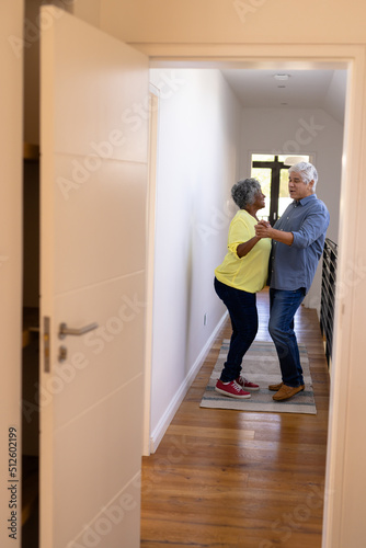 Cheerful multiracial senior friends dancing in corridor at nursing home seen through doorway